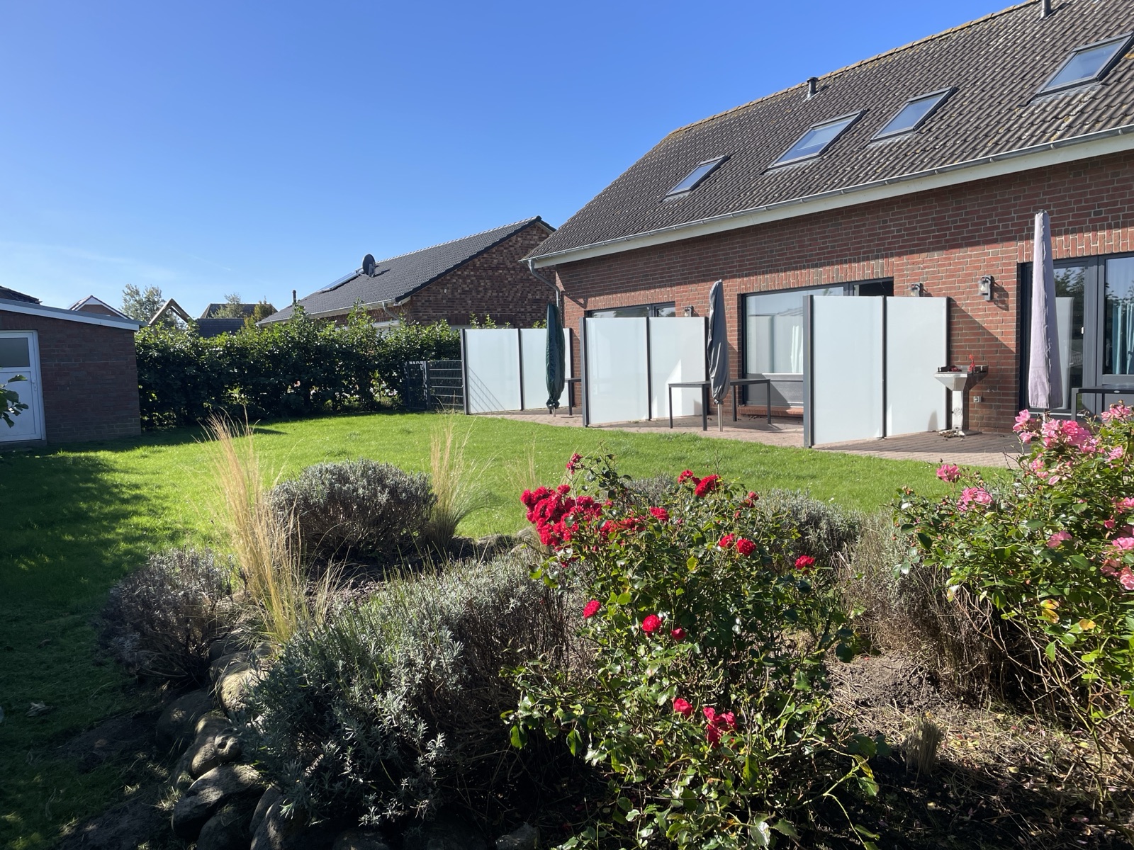 Garten mit Rasen, Blumen und Terrassen vor den Ferienwohnungen